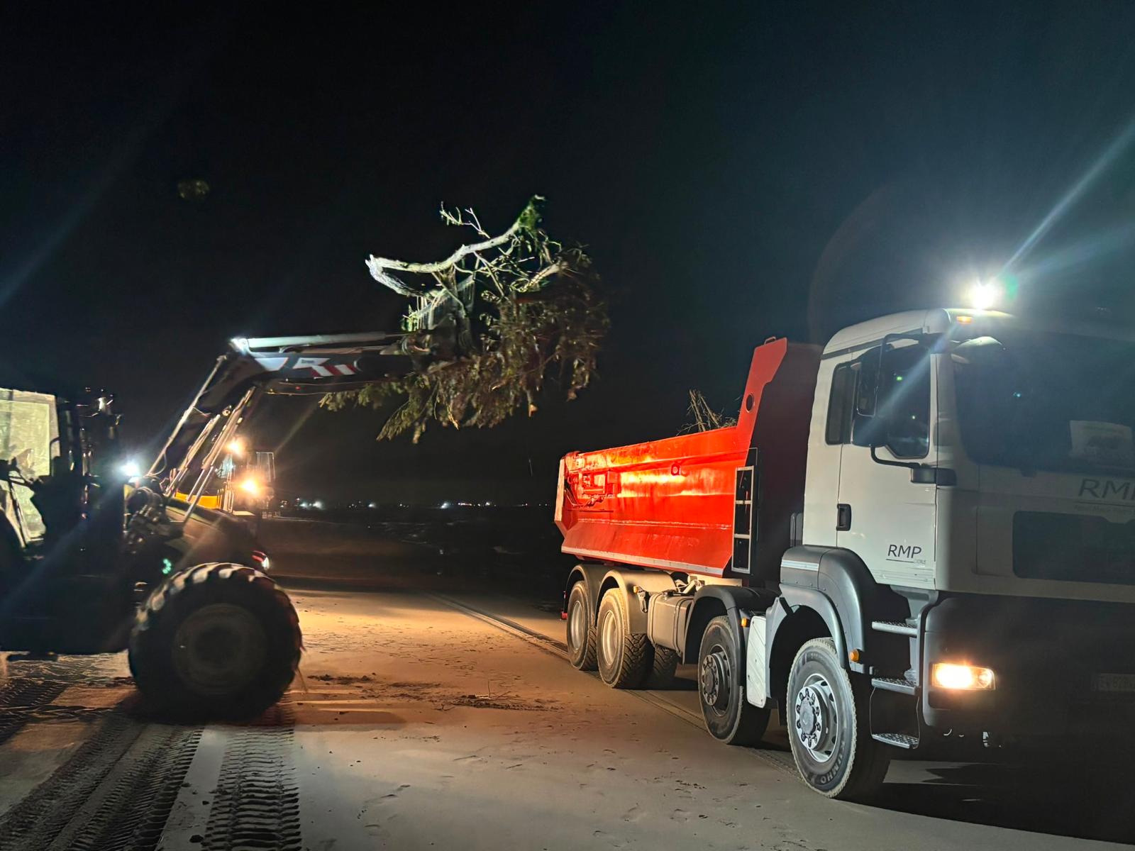 Pala meccanica carica ramaglie su un autocarro durante un intervento notturno